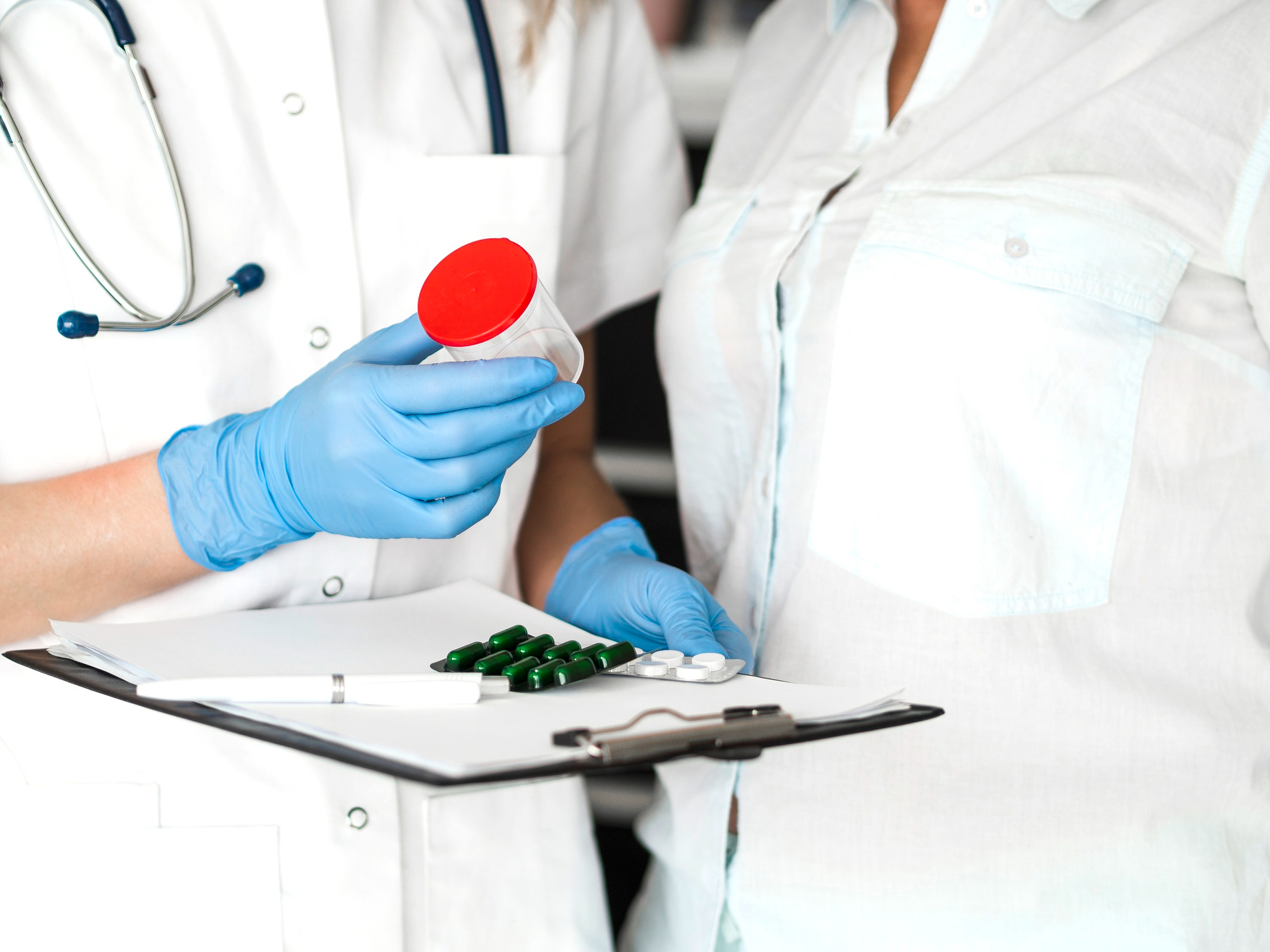 Doctor holding a sample container and pills while discussing with a patient.