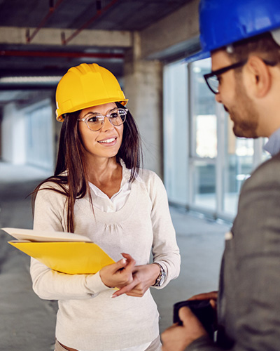 Female construction manager in a yellow hard hat talking to a colleague.