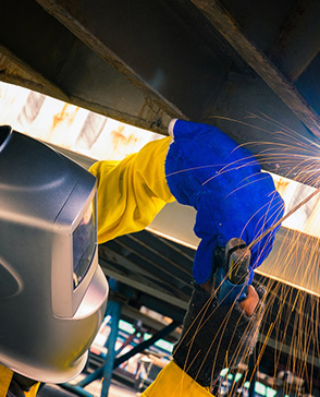 Worker welding metal with protective gear and sparks flying.